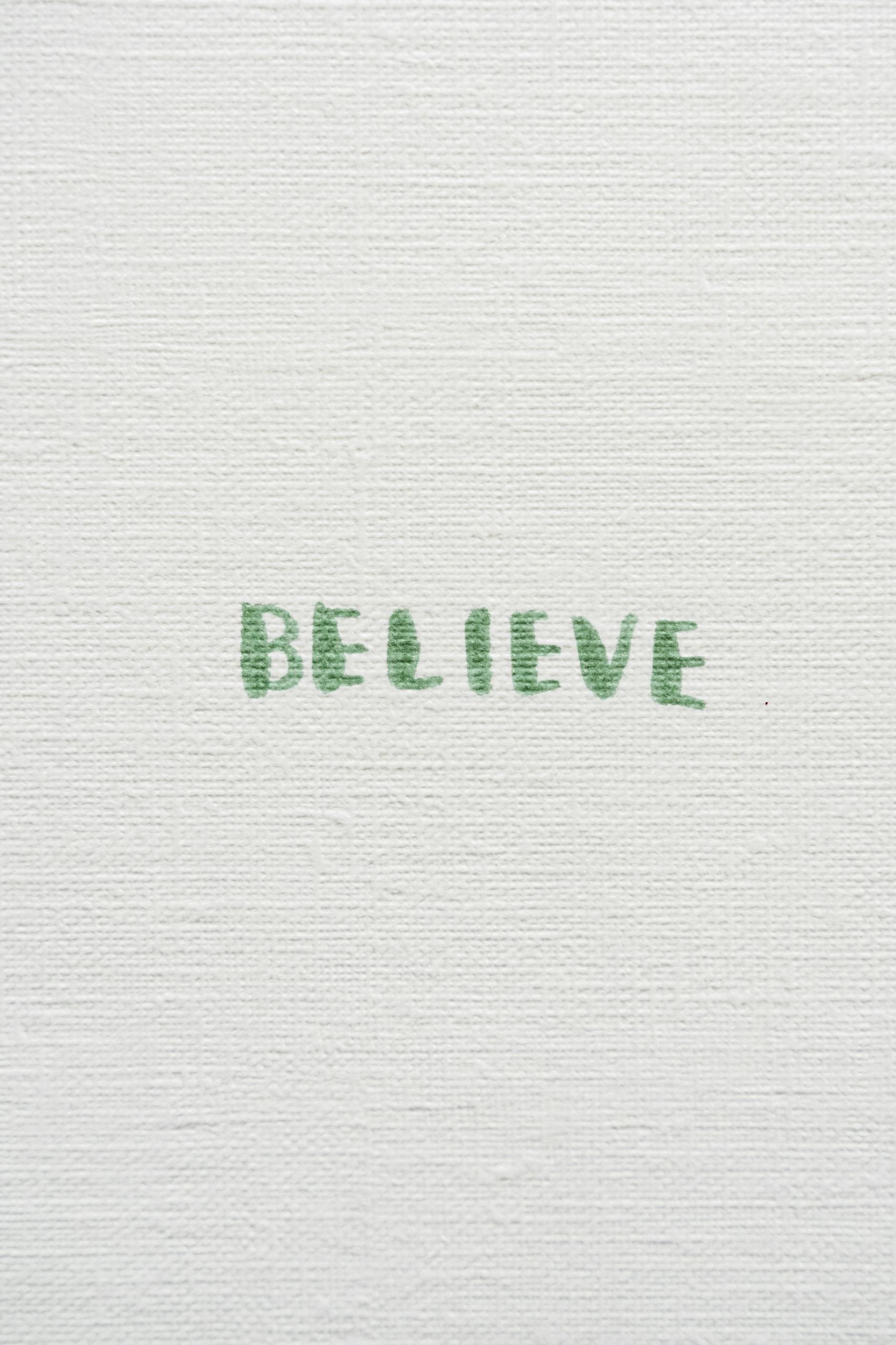 Green text 'BELIEVE' on textured white canvas background, close-up view.