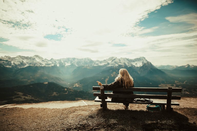 Woman enjoys a peaceful view of snow-capped mountains from a bench, capturing the essence of nature's serenity.