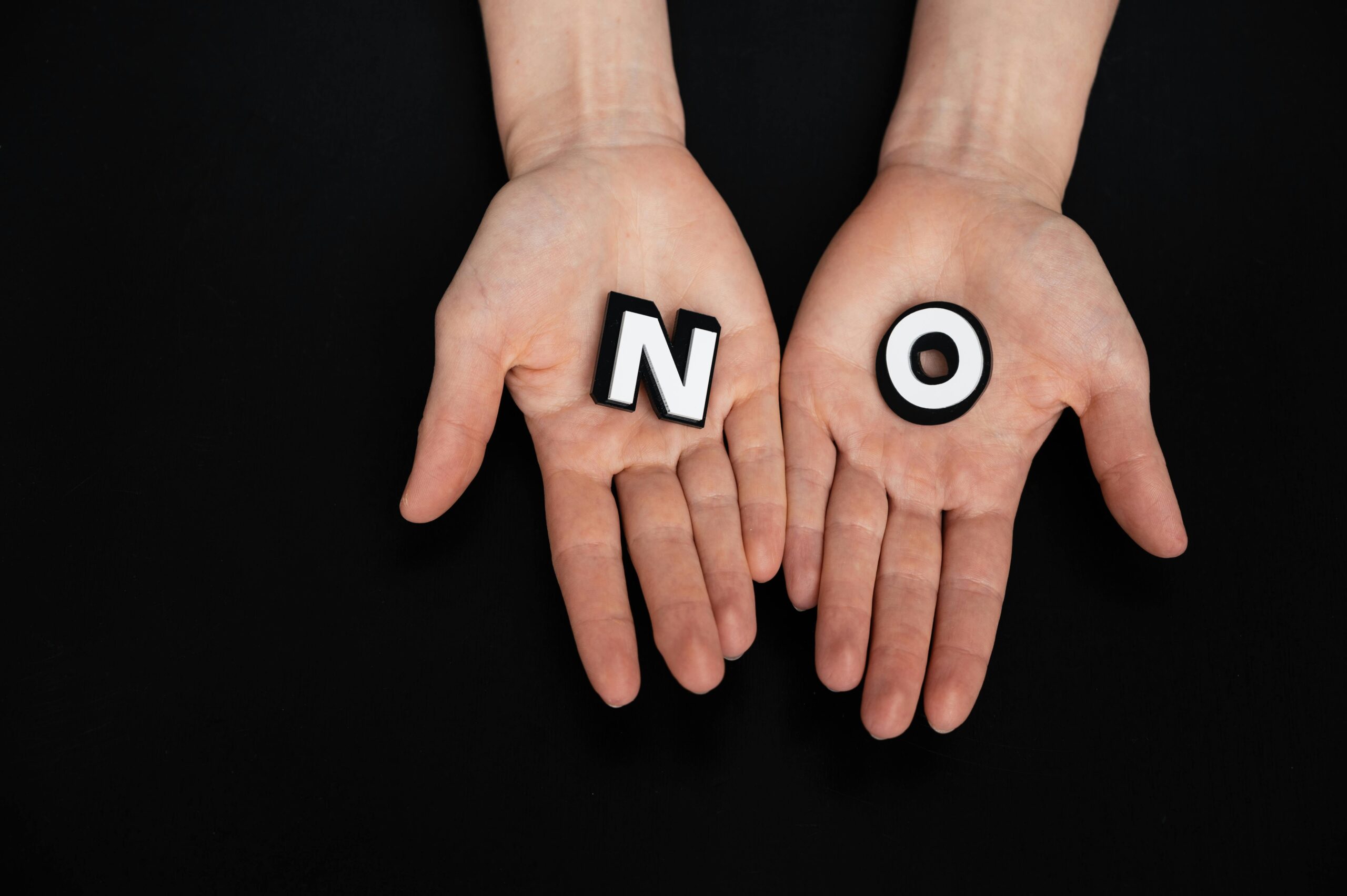 Close-up of open palms holding letters spelling 'NO' on a black background.